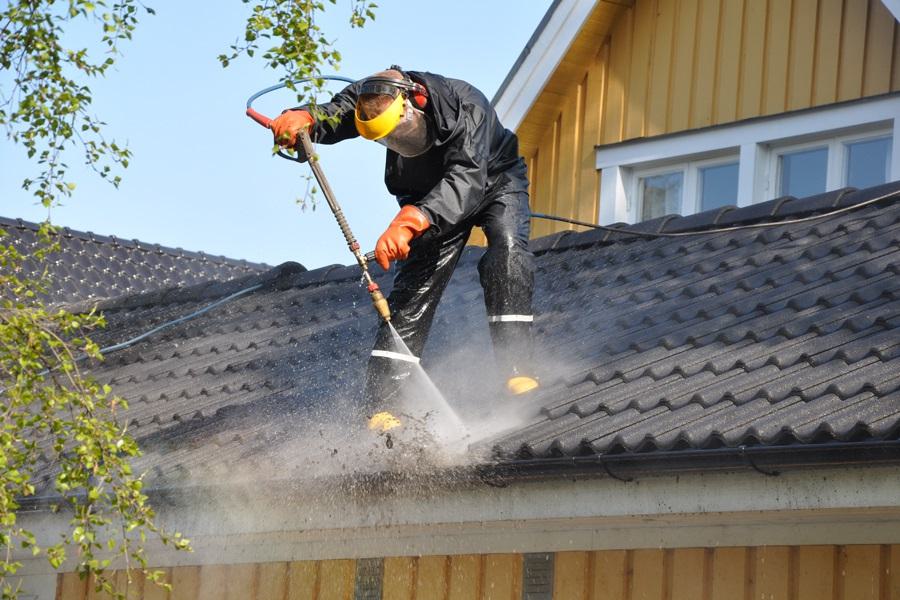 Worker pressure-cleaning a roof in protective gear.