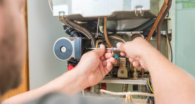 Close-up of a technician adjusting components inside a furnace unit with a screwdriver.